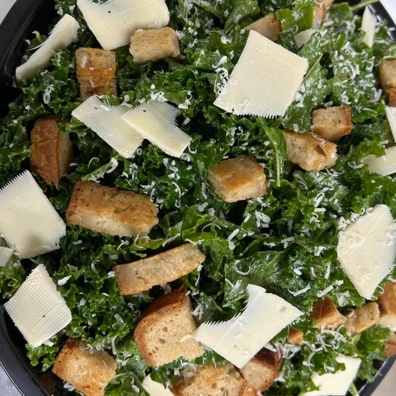 Close-up of a vibrant green kale salad topped with large parmesan shavings and golden croutons.
