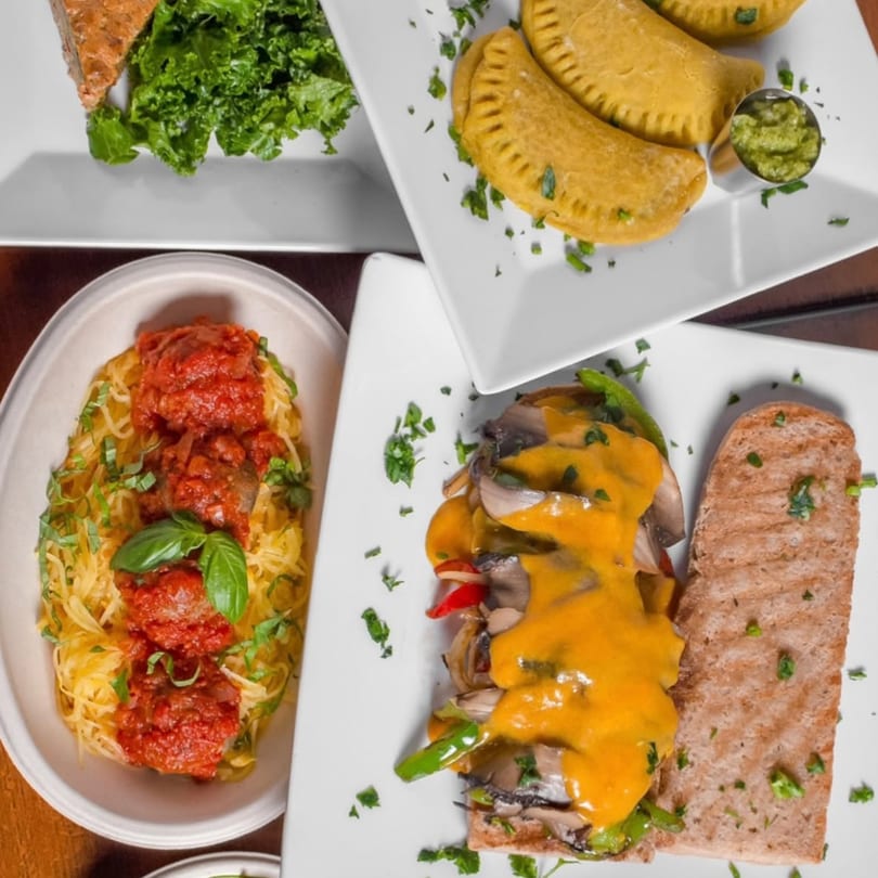 Overhead view of four vegan dishes: spaghetti squash, empanadas, a sandwich, and a salad.